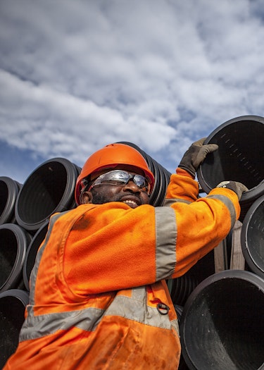 Portrait of civil engineer reaching up to stack of plastic piping
